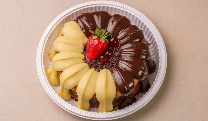 Foto vista de cima do bolo vulcão com chocolate branco servido em um prato descartável branco sobre uma mesa bege