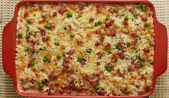 Foto bem aproximada de uma travessa vermelha, dentro da qual está a receita de Arroz de Forno, decorada com ervilhas e peito de peru
