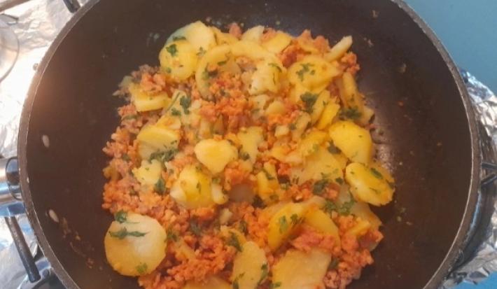 Fotografia de uma panela preta funda com batatas e calabresa moída.