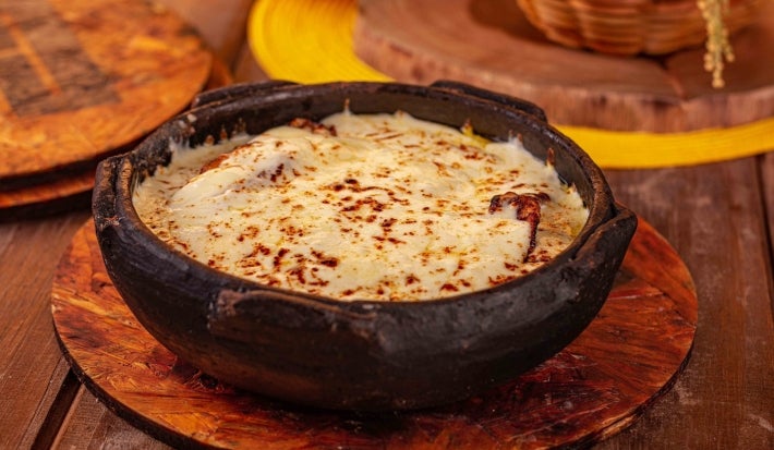 Em cima de uma mesa, há um refratário redondo queijo gratinado por cima.