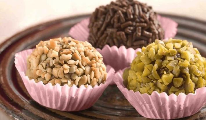 3 brigadeiros em forminhas lilás um com granulado por cima e os outros com castanhas picadas