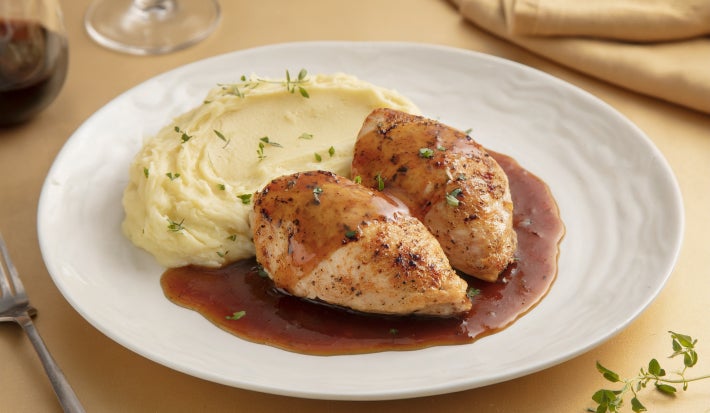 Pedaços de frango dourados servidos com purê cremoso de batata e molho escuro reduzido, apresentados em prato branco elegante