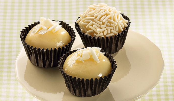 Fotografia em tons de branco, preto e verde de um paninho quadriculado verde e branco sobre ele um suporte branco com três brigadeiros de limão siciliano dentro de forminhas pretas.
