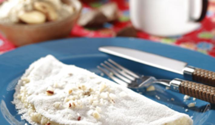 fotografia em tons de azul, branco e vermelho de uma bancada forrada com um pano vermelho e por cima um prato redondo azul com a tapioca e garfo e faca ao lado para servir.
