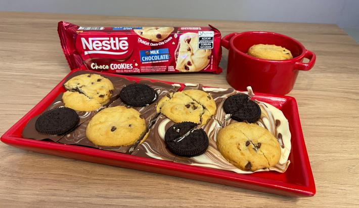 Fotografia de uma barra de chocolate mesclada com chocolate branco, sobre ela uma mistura de biscoitos e cookies.