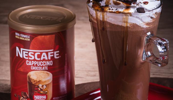 Foto da receita de cappuccino crocante servida em uma caneca alta de vidro sobre uma mesa de madeira