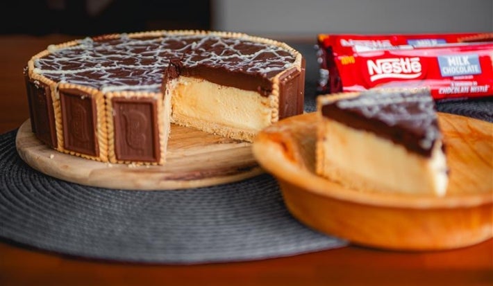 Fotografia de uma torta holandesa com um pedaço grande sobre um prato de madeira pequeno. A torta está em uma tábua redonda de madeira.