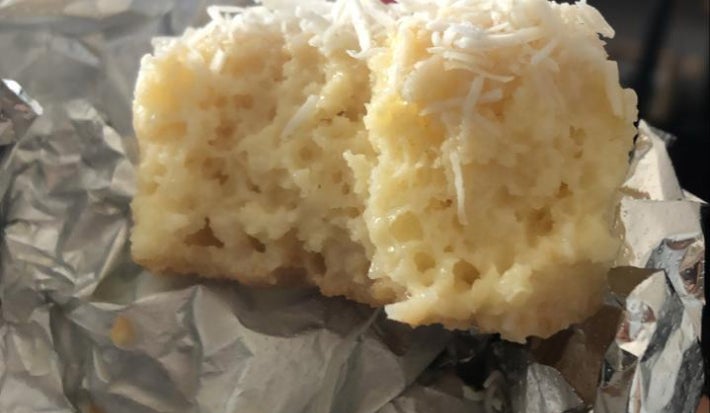 Bolo gelado de coco cortado ao meio, coberto com coco ralado e apoiado sobre papel-alumínio.