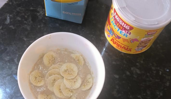 Fotografia de um recipiente branco fundo com um creme de farinha láctea com banana fatiada sobre uma bancada preta.