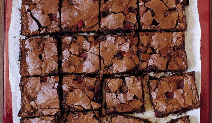 fotografia em tons de marrom e branco de uma bancada vista de cima, contém um pano branco e por cima pedaços quadrados de bolo de chocolate
