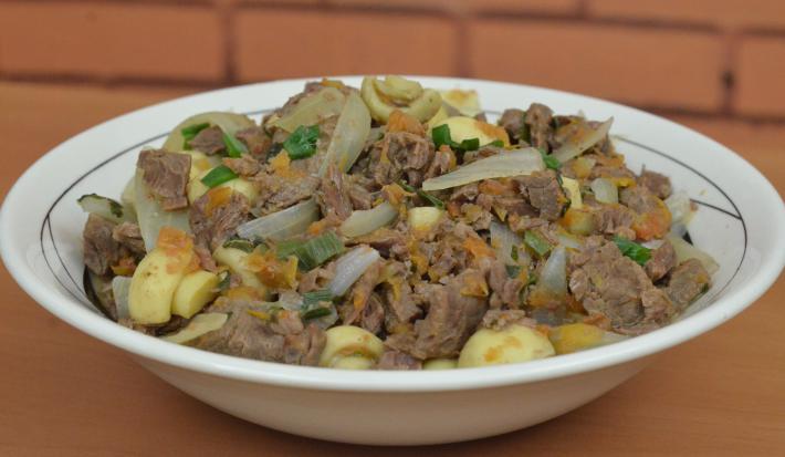 Fotografia em tons de marrom de uma bancada marrom com um prato branco, sobre ele carne de panela.