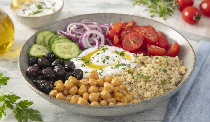 imagem mostra bowl mediterrâneo com quinoa, grão-de-bico, tomate-cereja, pepino, cebola roxa e azeitonas pretas, servido com molho de iogurte e Fiber Mais® Limão + Colágeno.