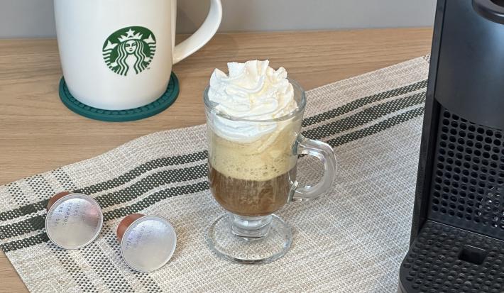 Fotografia em tons de verde escuro com uma xícara com a bebida de starbucks com chantilly, um paninho verde.