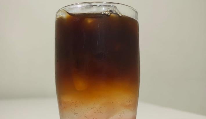 Foto da receita de espresso tonica com amora servida em um copo de vidro alto sobre uma mesa branca