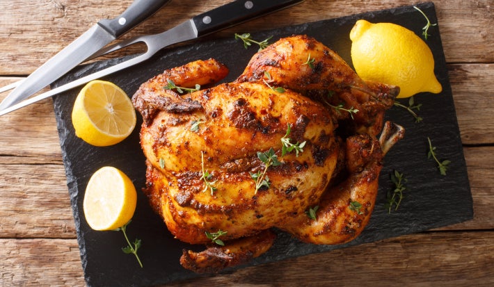Imagem de uma tábua com um peru assado com ervas, limões ao lado e um garfo e faca.