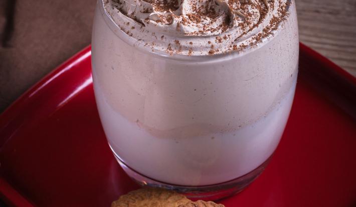 Foto da receita de cappuccino super cremoso  sobre uma louça vermelha em cima de uma mesa de madeira vista de cima