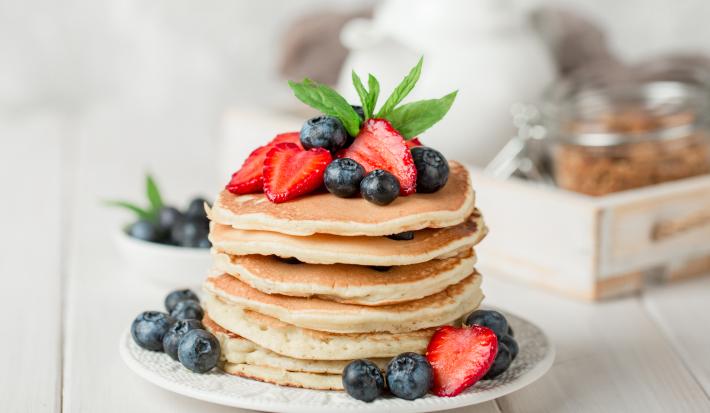 Fotografia de uma torre de panquecas e pedaços de frutas.
