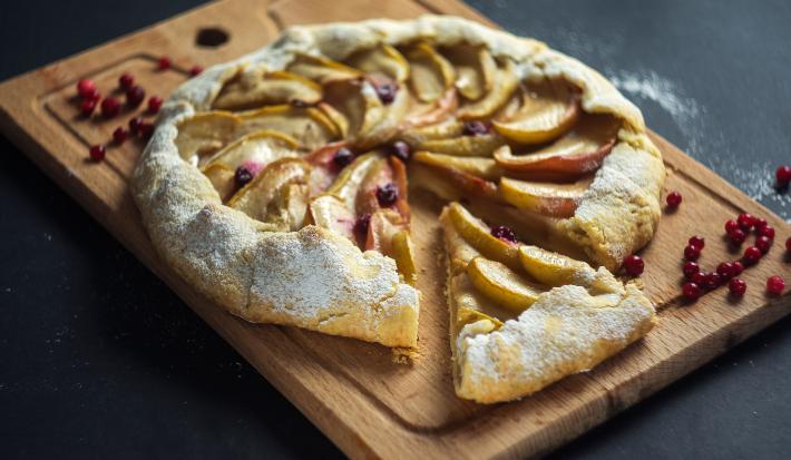 Fotografia em tons de marrom com uma tábua de madeira ao centro. Em cima da tábua existe uma torta rústica de maçã com a massa feita de NESTLÉ Farinha de aveia.