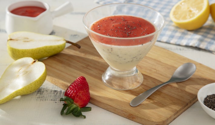 Fotografia em tons claros com um pote de vidro ao centro. Dentro do pote existe um pudim de pera coberto com uma geleia de morango.