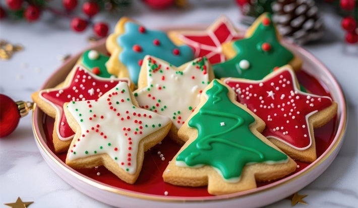 Em cima de uma mesa, prato redondo com biscoitos em formatos de estrela e árvore de natal, decorados com glacê colorido e confeitos de bolinhas coloridas.