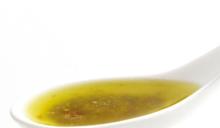 Fotografia em tons de amarelo em uma mesa e fundo brancos, com uma colher de molho e dentro o molho vinagrete.