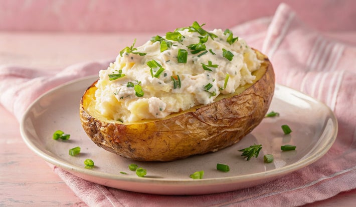 Imagem mostra um prato com uma batata grande cortada ao meio e um creme por cima recheando-a