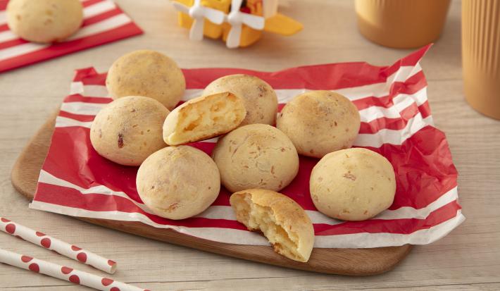 Fotografia em tons de vermelho com vários pães de queijo feitos com NINHO Primeira Infância ao centro.