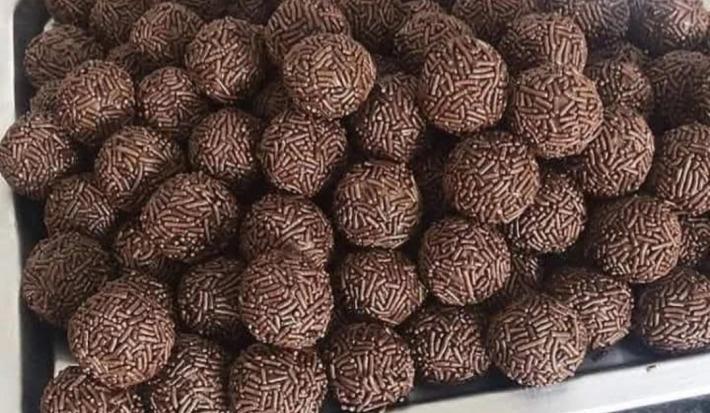 Fotografia de vários brigadeiros de café passados no granulado tradicional. Os brigadeiros estão dentro de uma forma grande retangular de alumínio.