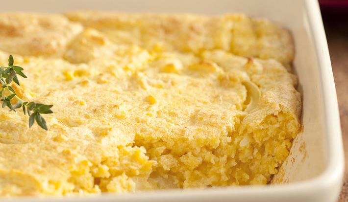 Fotografia em tons de branco e amarelo de uma bancada de madeira com um recipiente retangular branco com a sopa paraguaia.