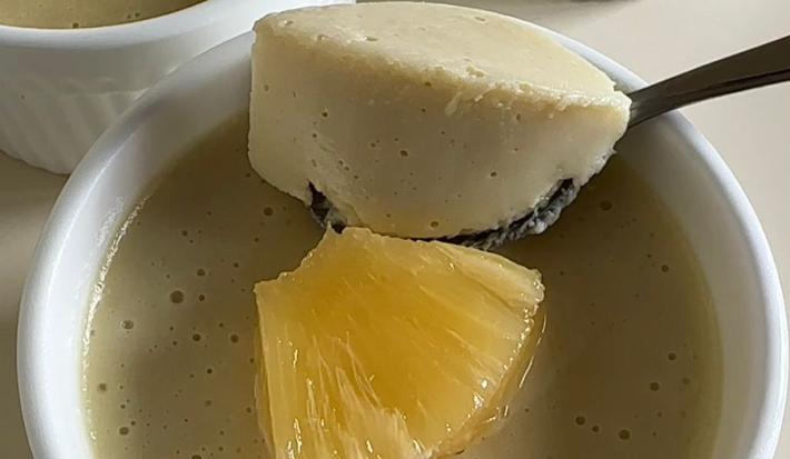 Fotografia em tons claros de três ramekins brancos com mousse de abacaxi com um pedaço da fruta decorando por cima. O ramekin no centro da foto tem uma colher segurando um pouco da mousse.