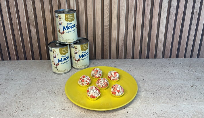 Prato amarelo com docinhos decorados com confeitos de coração vermelhos e brancos, com Leite Moça ao fundo.