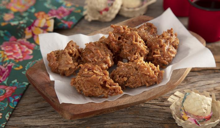 Foto da receita de Quebra-queixo. Observa-se tecidos com a temática junina e chapéuzinhos de palha como decoração na foto e, ao meio, uma tábua de madeira com 7 quebra-queixos.