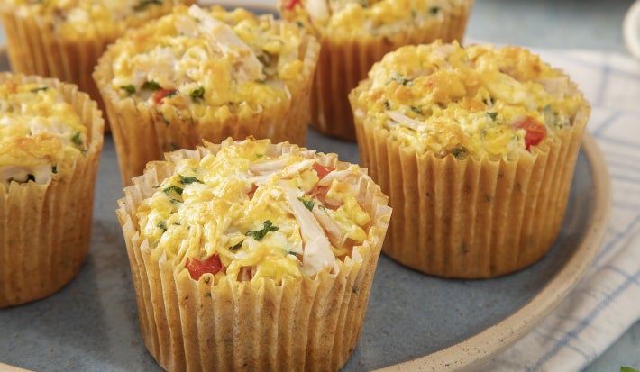 fotografia em tons claros com pequenas tortas de frango ao centro. cada tortinha é feita em uma forma de cupcake e possui frango desfiado, tomate e ervas frescas