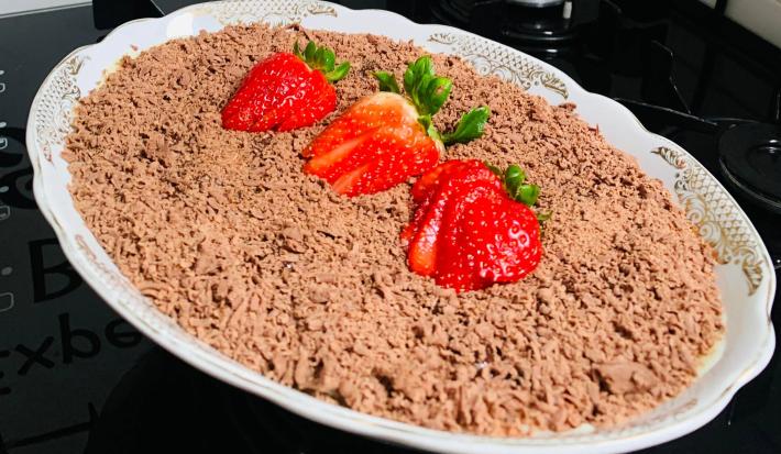 Foto aproximada da receita de bombom de morango na travessa fácil, servido em uma travessa branca de porcelana, decorado com raspas de chocolate ao leite por cima e morangos fatiados