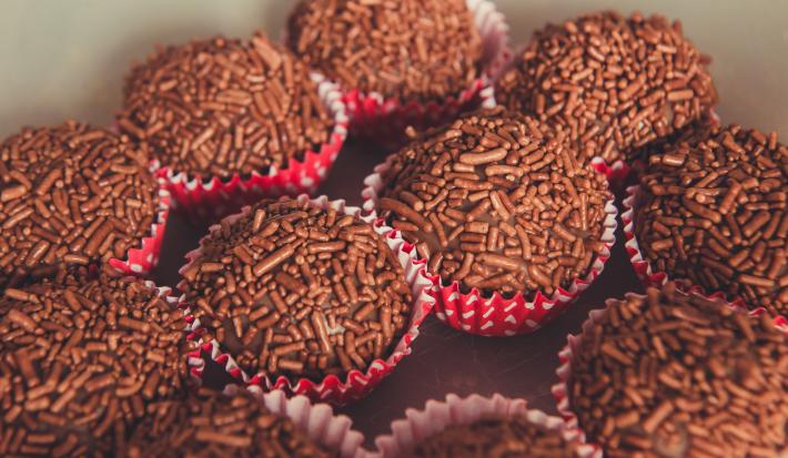 Fotografia de várias unidades de brigadeiro, passados no granulado dentro de forminhas vermelhas com bolinhas brancas.