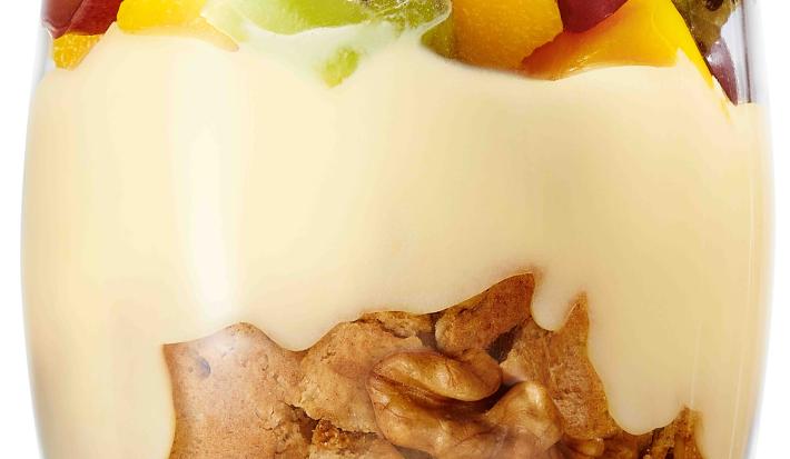 fotografia tirada de um copo transparente com biscoitos triturados, leite MOÇA e frutas por cima.