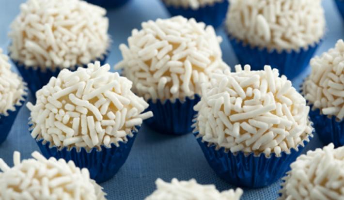 Fotografia em tons de branco e azul de vários brigadeiros em forminhas azuis metalizadas com granulado branco.