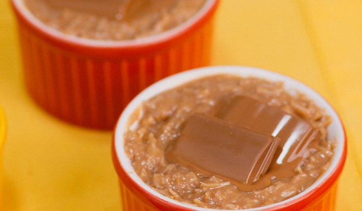 Cocada cremosa em ramequim vermelho, coberta com pedaço de chocolate recheado, sobre toalha amarela.