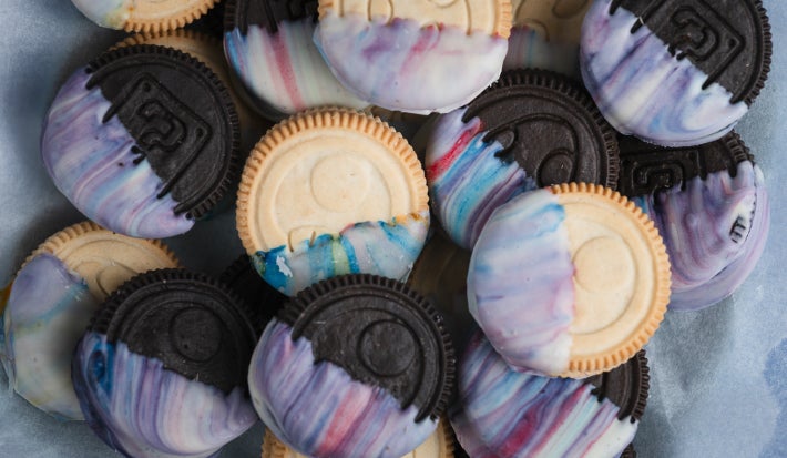 Detalhe de biscoitos claros e escuros cobertos com creme marmorizado azul, rosa e branco, empilhados sobre papel manteiga.