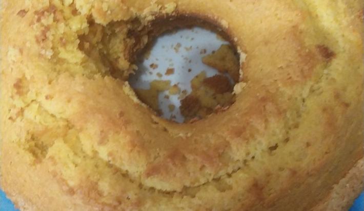 Fotografia de um bolo inteiro de fubá sem lactose. O bolo está sobre um prato azul raso.