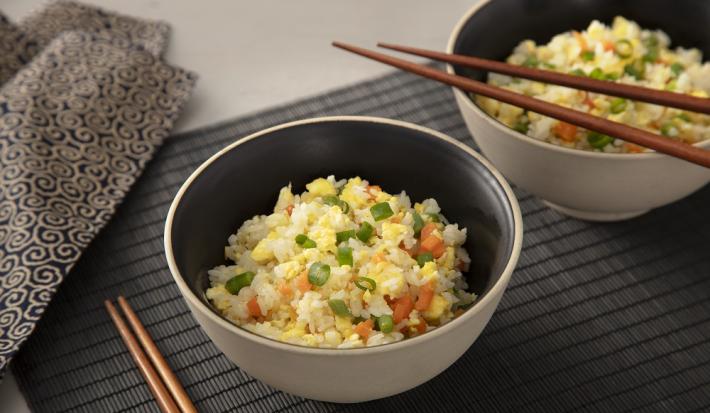 Foto da receita de yakimeshi. Observa-se duas tigelas com o arroz dentro sobre uma esteira preta e dois hashis apoiados.