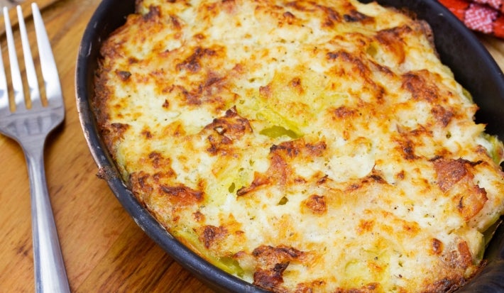 Em cima de uma mesa, refratário preto com queijo gratinado, ao lado, garfo.