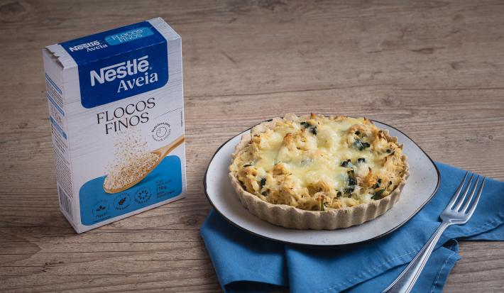 Foto da receita de quiche de aveia com espinafre servida em um grande prato desforme branco sobre um pano azul em cima de uma mesa de madeira