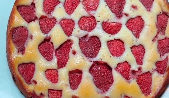 Foto da receita de Bolo de Iogurte e Morango. Observa-se um bolo redondo assado com morangos cortados ao meio no topo.