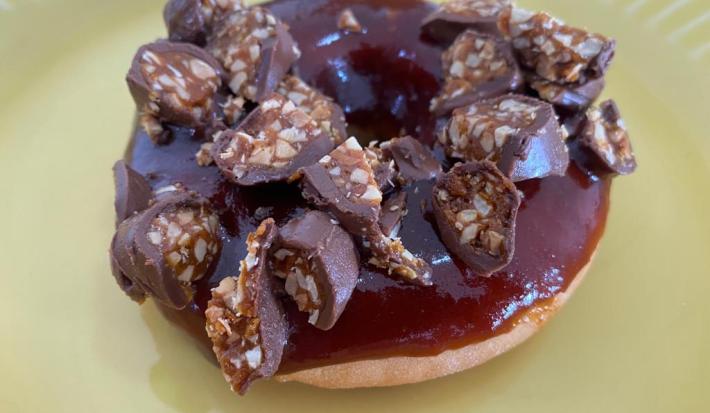 Fotografia de um donuts coberto com caramelo e um pedaço de um bombom de chocolate com caramelo por cima.