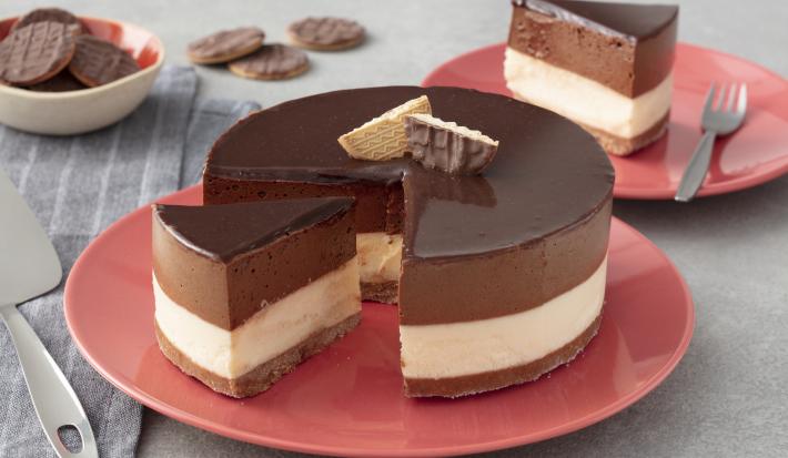 Fotografia em tons de vermelho em uma bancada de madeira cinza, um pano cinza listrado, um prato vermelho redondo raso com a torta mousse de chocolate com recheio de sorvete de creme e cobertura de chocolate.