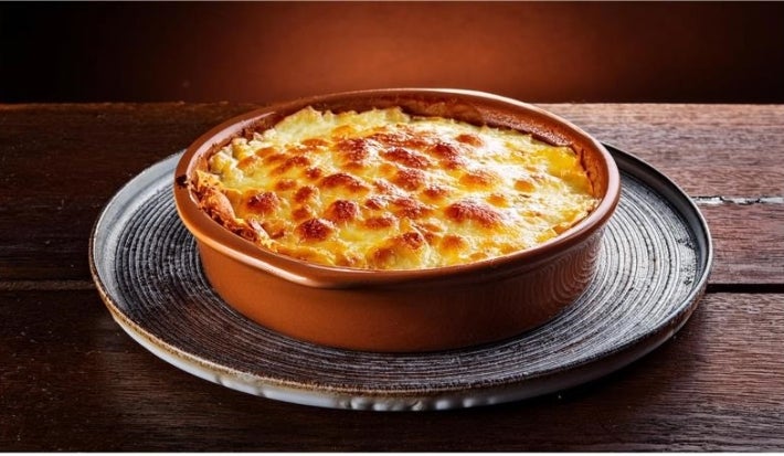 Em cima de uma mesa, há um refratário redondo queijo gratinado com crostas de queijo.