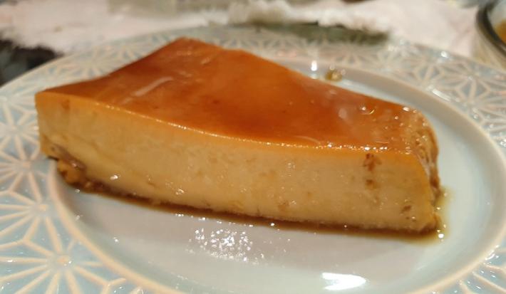 Foto de uma fatia da receita de pudim de doce de leite com calda de café servida sobre um prato de porcelana azul claro com adornos em branco