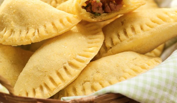 em um cesto com um pano em tons de verde claro contém diversos pasteis e dois abertos recheados com linguiça