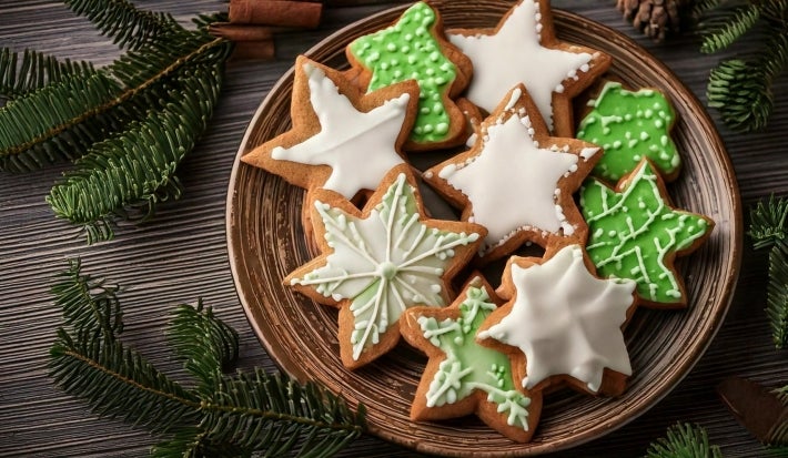 Em cima de uma mesa, prato redondo com biscoitos em forma de estrelas, decorado com glacê branco e verde, e confeitos redondos brancos.